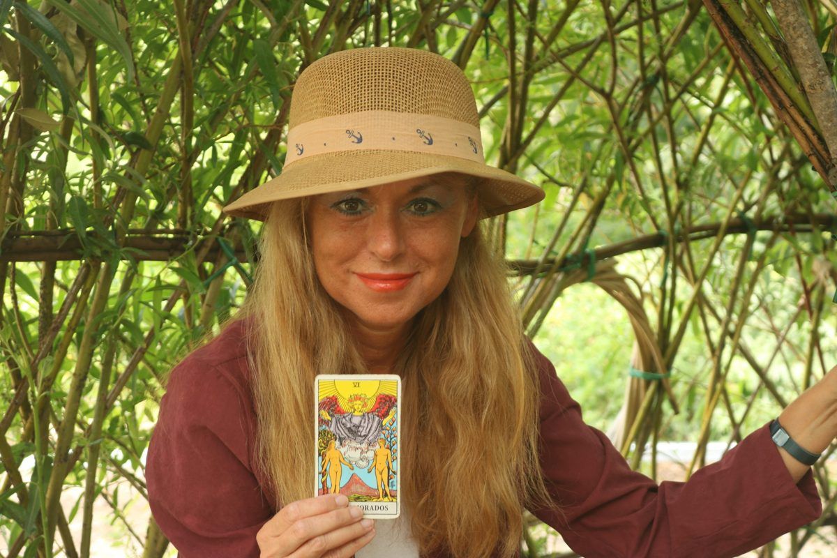 Cristina sonriendo, con sombrero, mostrando la carta de Los Enamorados