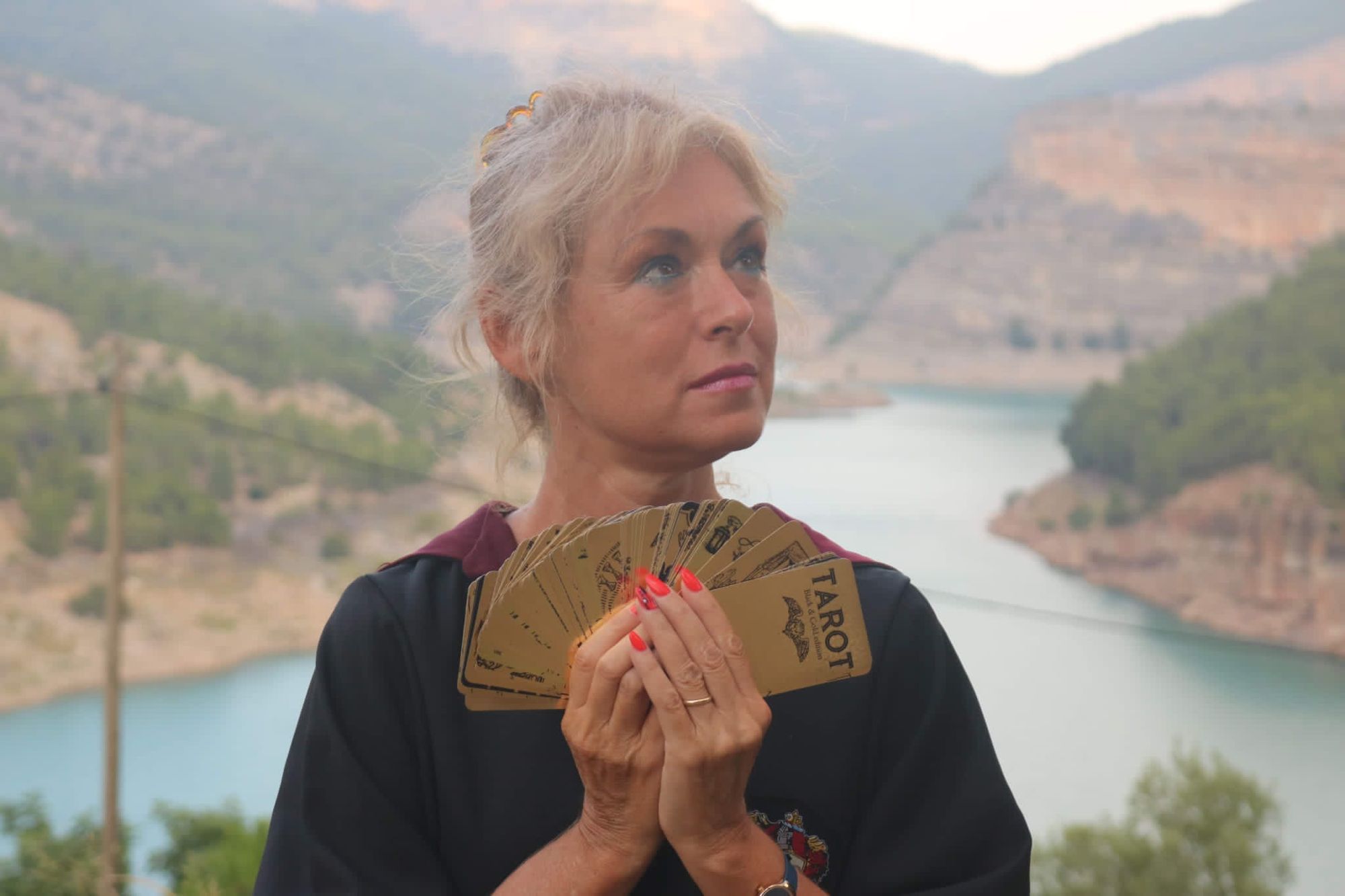Cristina Noferini con su baraja dorada entre las manos, mirando al horizonte sobre un lago entre montañas al atardecer